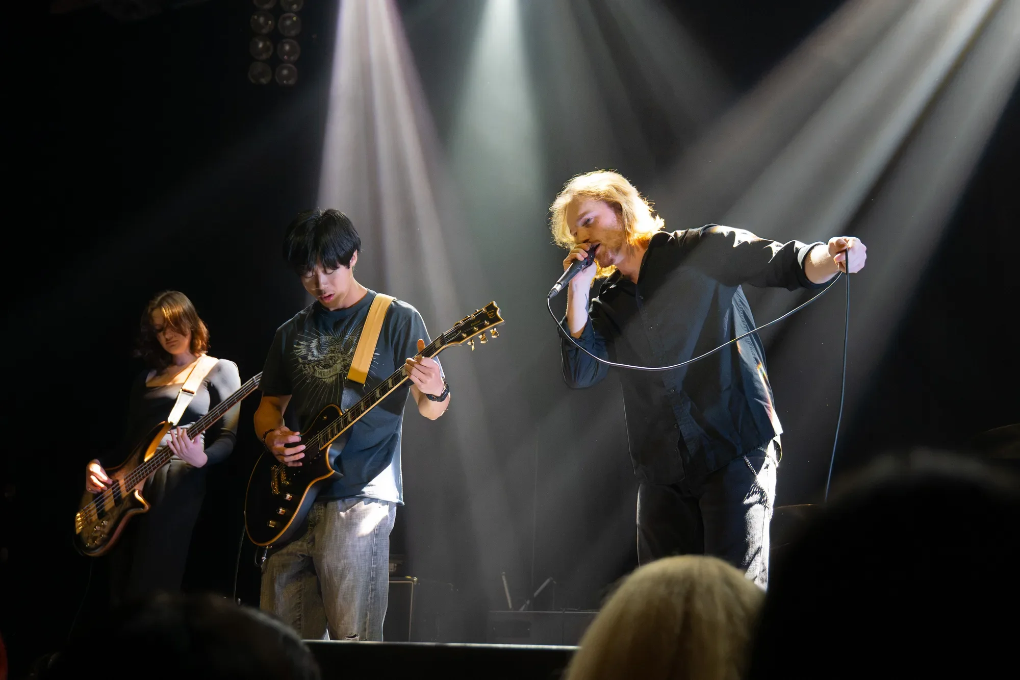 The members of In Pieces perform passionately as white beams of light shower down upon them.