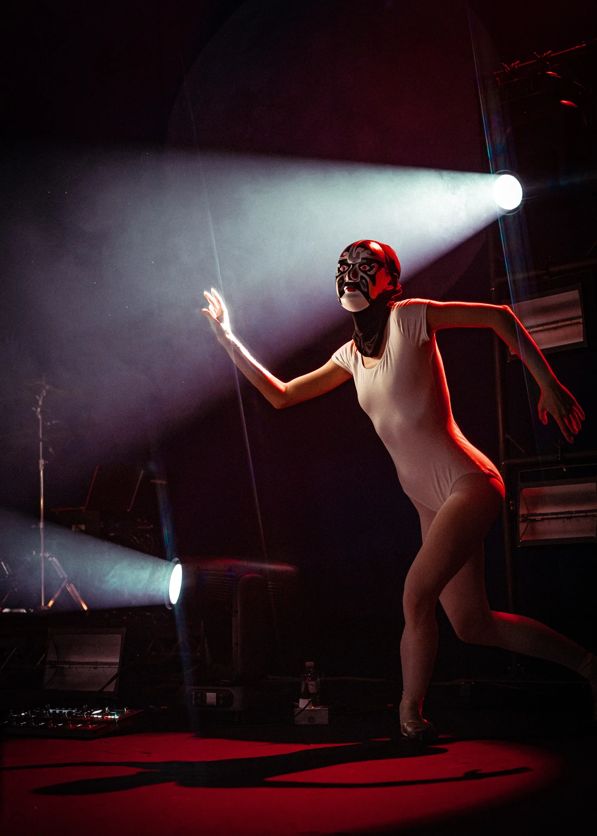 One of Emei’s masked dancers in a white bodysuit moves through white beams and red stage lighting at Vogue Theatre.