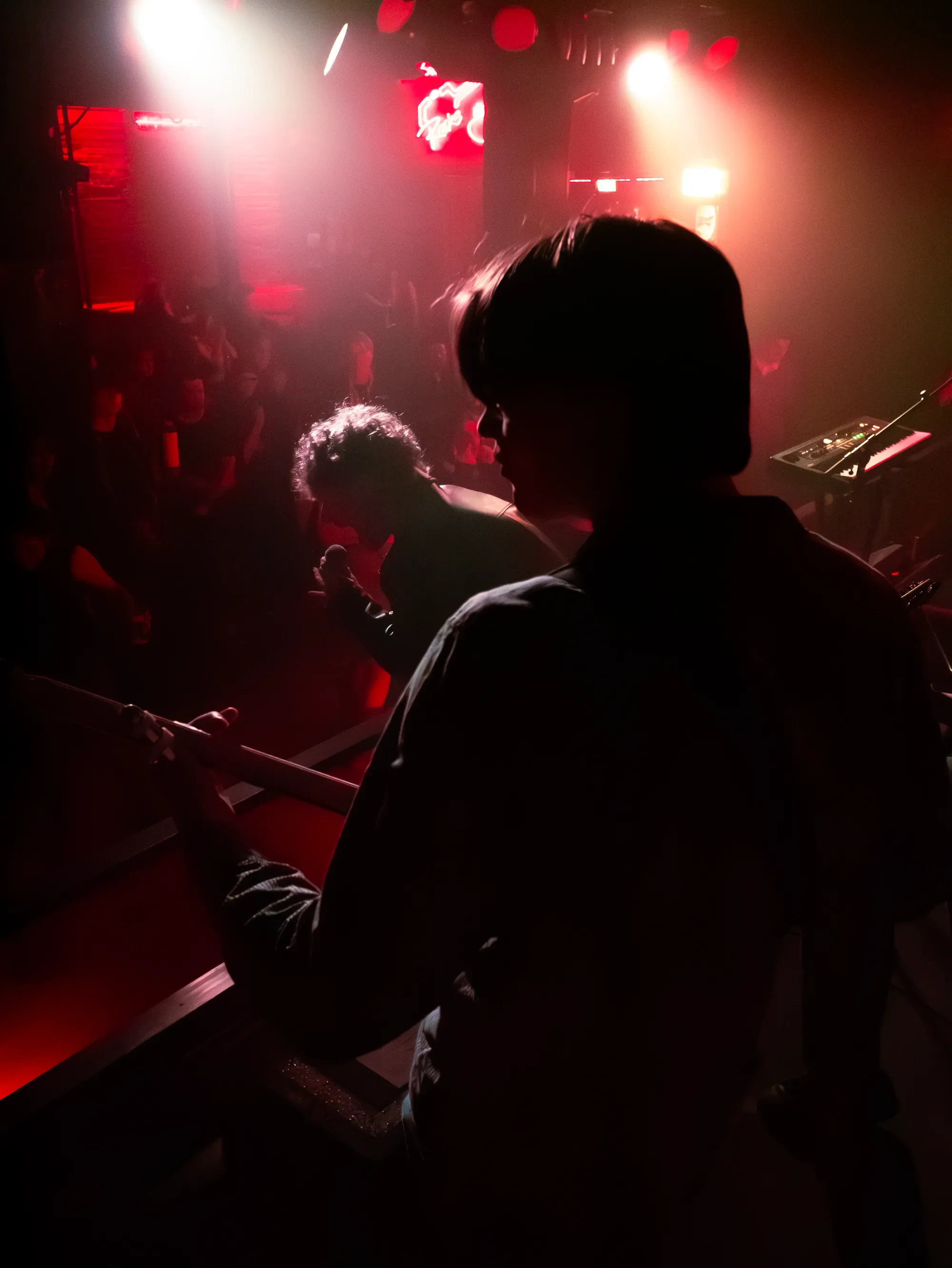 MAGNETIQ performing in red light, with a musician silhouetted in the foreground.