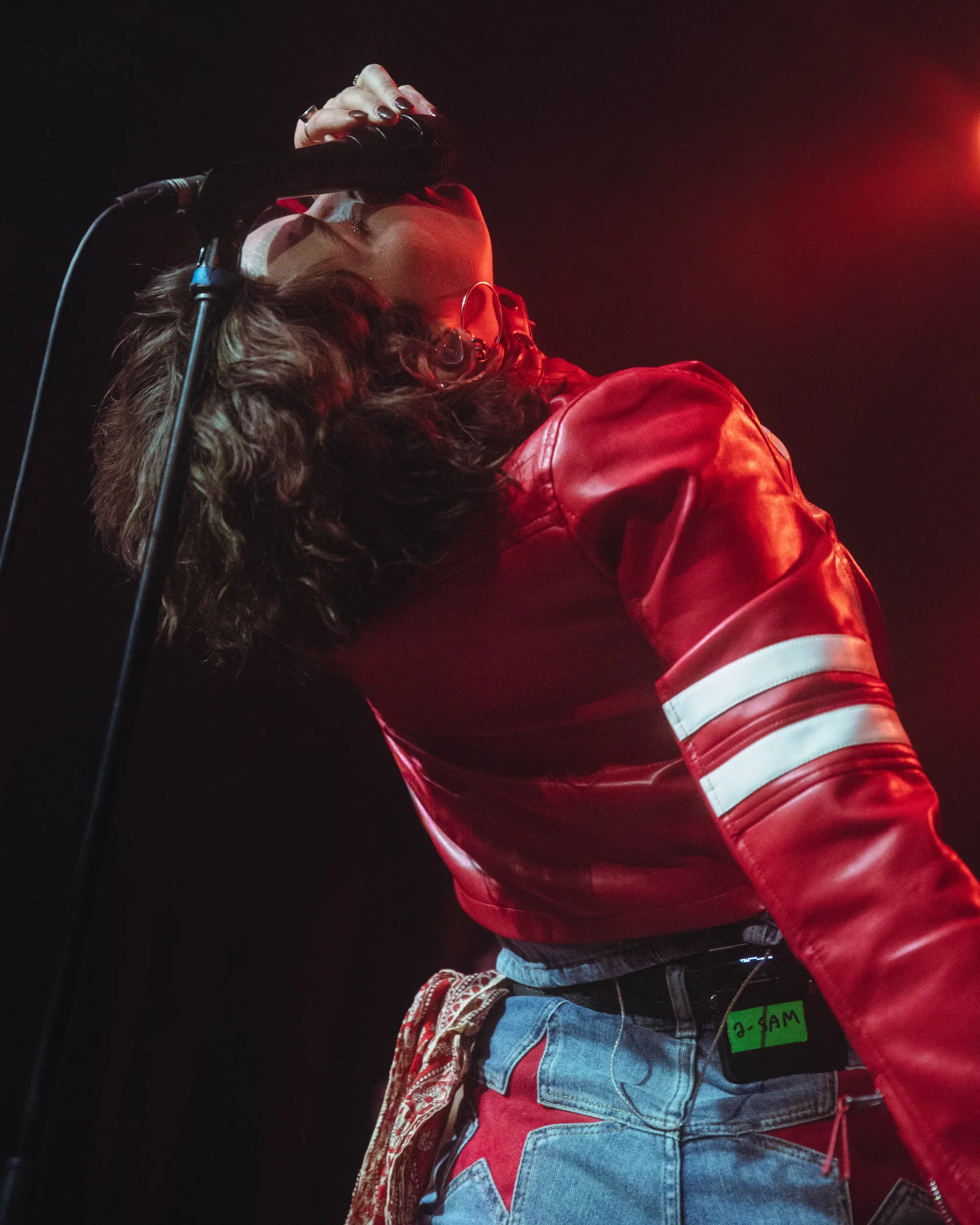 Sammy Rae singing into a microphone with her head tilted back under red light.